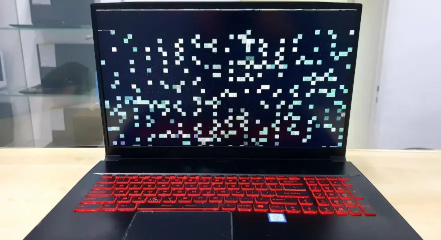 Laptop z artefaktami na ekranie, wskazującymi na problemy z kartą graficzną. Klawiatura podświetlona na czerwono.