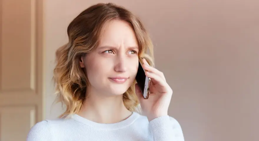 Zmarszczona kobieta rozmawia przez telefon, próbując dowiedzieć się, jak zwiększyć głośność w telefonie, bo rozmówca mówi za cicho.