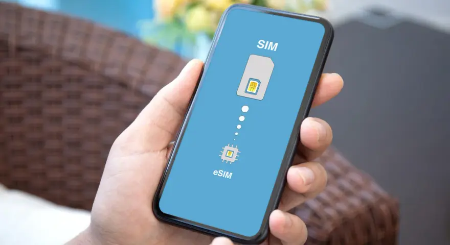 Dłoń trzyma smartfon z wyświetloną grafiką porównującą tradycyjną kartę SIM z technologią eSIM.