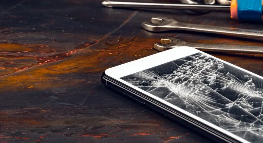 Zepsuty ekran telefonu leży obok narzędzi. Pęknięcia tworzą pajęczynę na szkle.