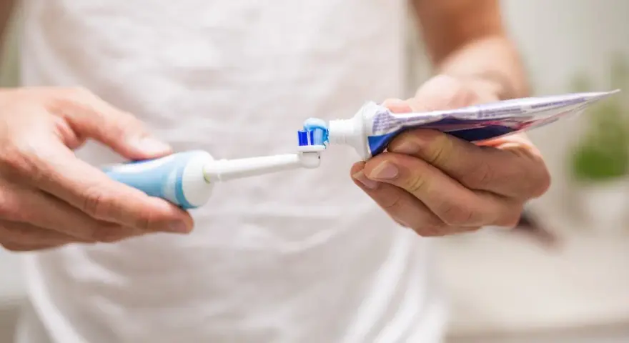 Przygotowanie do mycia zębów szczoteczką soniczną: nakładanie pasty na główkę.