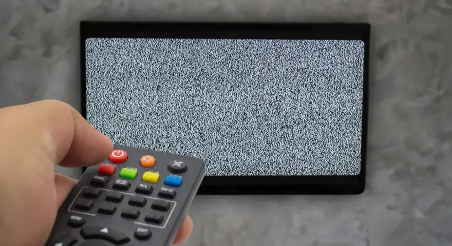 Ręka trzyma pilot dekodera, celując w ekran telewizora z zakłóceniami. Czas na naukę, jak sparować pilot dekodera z telewizorem.