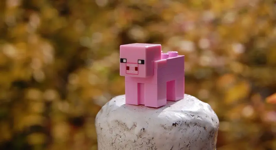 Różowa świnka z klocków Minecraft na białym postumencie. Może to być inspiracja do najlepszych modów do Minecraft, które dodają nowe zwierzęta.