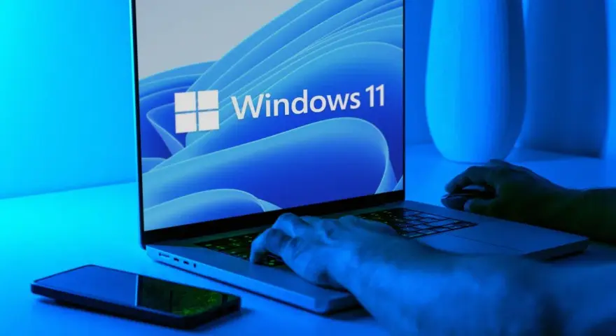 Ręce na klawiaturze laptopa z logo Windows 11. Dowiedz się, jak wejść do BIOS-u Windows 11, aby dostosować ustawienia.