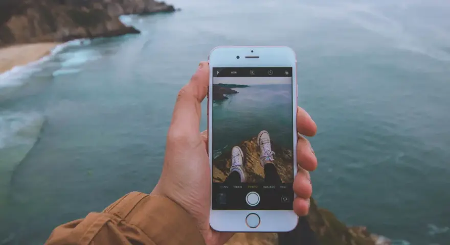 Dłoń trzyma iPhone'a 15, na ekranie widok klifów i oceanu. Czy iPhone 15 jest wodoszczelny? To pytanie zadaje sobie wielu podróżników.