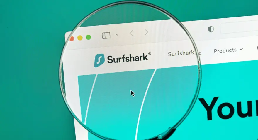 Lupa w telefonie powiększa logo Surfshark i fragment strony internetowej.