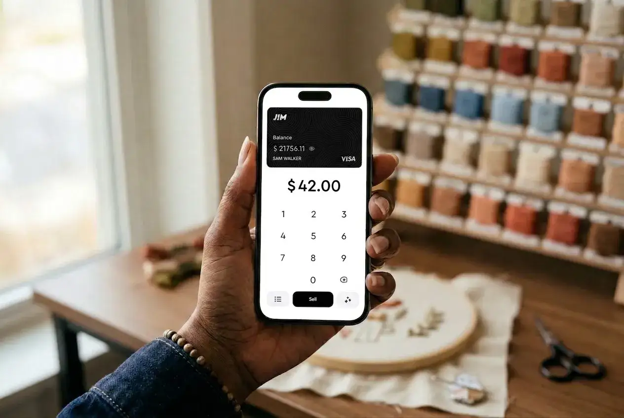 Dłoń trzyma smartfon z włączonym NFC w telefonie, wyświetlający aplikację płatniczą z kwotą 42.00$. W tle widać regał z kolorowymi nićmi.