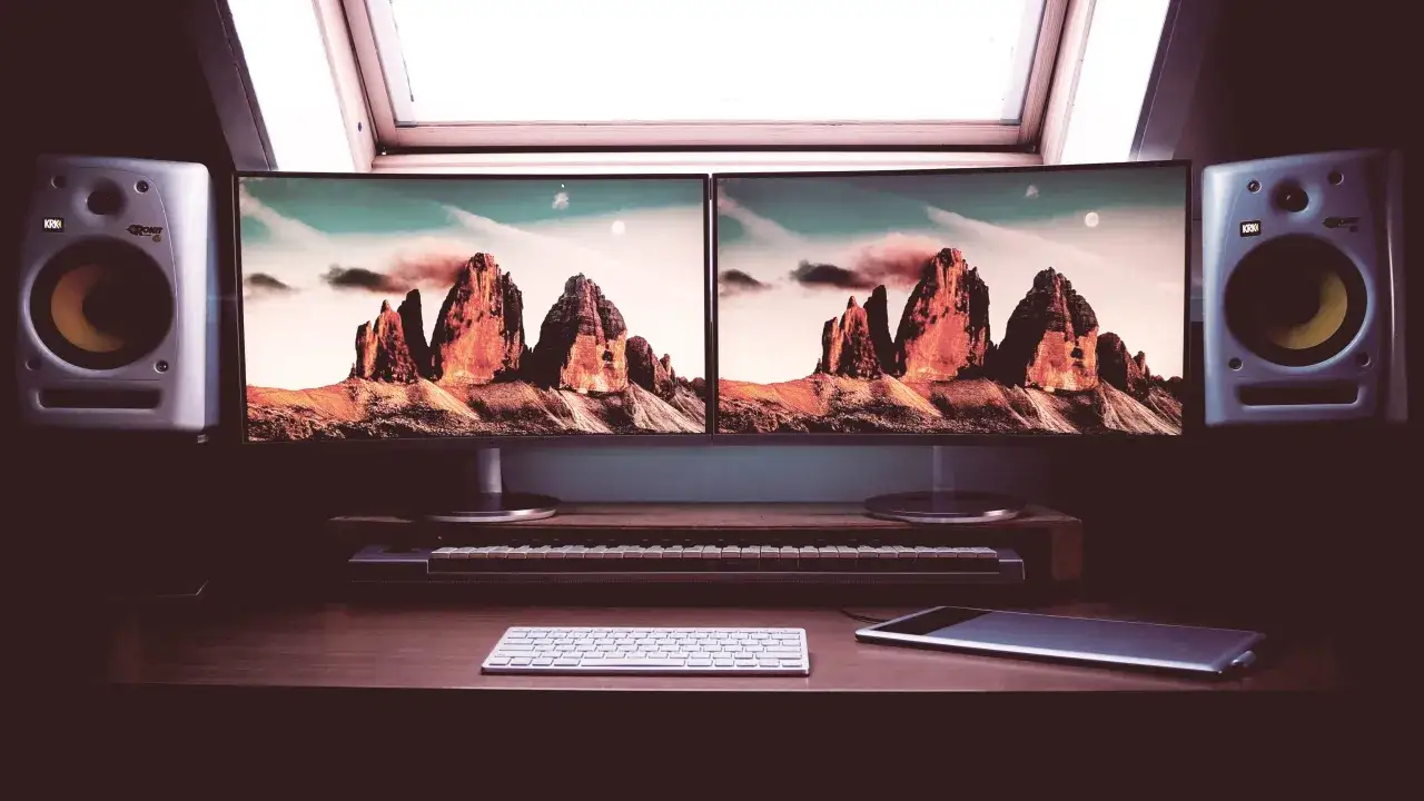 Stacja robocza z dwoma monitorami wyświetlającymi g&oacute;ry, klawiaturą, tabletem i głośnikami. Dowiedz się, jak podłączyć dwa monitory do laptopa, aby uzyskać podobny widok.
